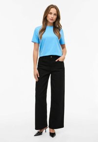 Jasnoniebieska bawełniana koszulka z krótkim rękawem, zestawiona z czarnymi szerokimi spodniami z wysokim stanem oraz czarnymi szpilkami z ostrym noskiem.