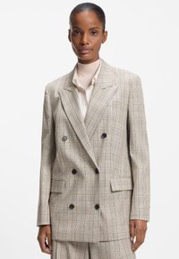 Beige ternet dobbeltradet blazer med sorte knapper, store revers og to forlommer. Glat stof med en struktureret pasform.