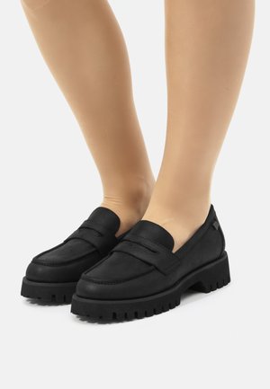 Mocasines negros de ante texturizado con suela de goma gruesa. Presentan una correa decorativa y costuras en la parte superior.