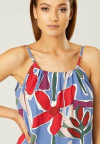 Mouwloze top met bloemenpatroon op een blauwe achtergrond, abstracte rode en groene bloemen, gathered halslijn en dunne schouderbandjes.