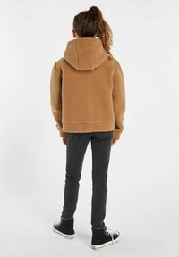 Felpa con cappuccio beige, dotata di un ampio cappuccio, superficie texturizzata e orlo a coste, abbinata a jeans skinny scuri e sneaker alte nere.