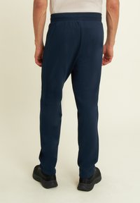 Pantalones de chándal azul marino hechos de una tela suave con un ajuste ajustado, cinturilla elástica y detalles en las costuras laterales, combinados con zapatillas deportivas negras.