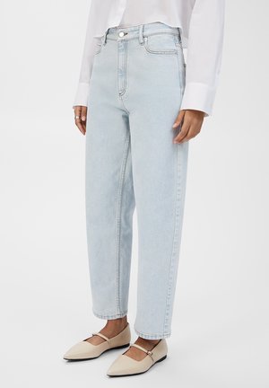 Lyseblå høy midje jeans med rett ben, klassisk fem-lomme design og broderte detaljer, parret med beige flate sko.
