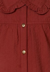 Koszula w kolorze rdzy z falbaniastym kołnierzykiem, z guzikami z przodu i teksturowanym materiałem. Zawiera złote guziki do zapięcia.