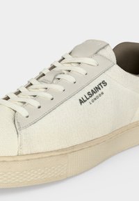 Λευκό χαμηλό αθλητικό παπούτσι με κορδόνια, υφασμάτινη επιφάνεια, λαστιχένια σόλα και λογότυπο "ALLSAINTS LONDON" στο πλάι.