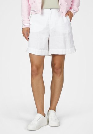 Person wearing white cuffed shorts, white sneakers, and a pink jacket with hands in pockets, standing on a white background.