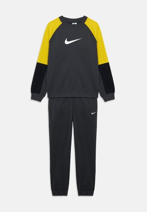 Sudadera gris con acentos amarillos y negros, con un logo blanco de Nike. Combinada con pantalones de chándal grises a juego, con puños elásticos incluidos.