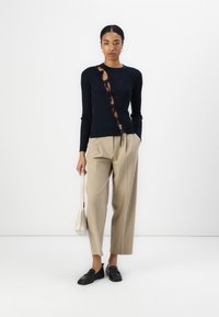 Top de manga larga acanalado en color marino con cortes laterales y detalle de cordones, combinado con pantalones de talle beige y mocasines negros. Pequeño bolso blanco.