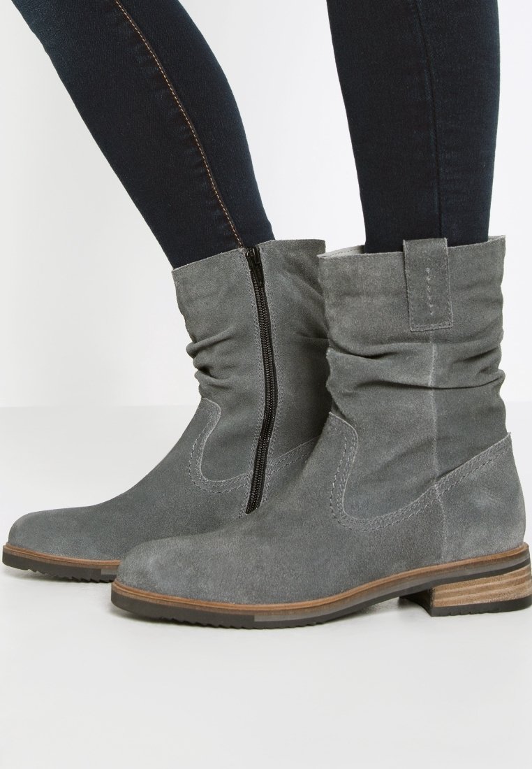 Des bottines en suède gris présentent un design décontracté avec une fermeture éclair sur le côté, un talon en bois marron et de subtils accents de coutures sur les côtés.