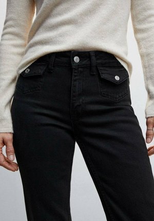 Jeans de mezclilla negra con un diseño ajustado, que presentan herrajes de botón plateado y bolsillos frontales. La tela tiene una textura suave.