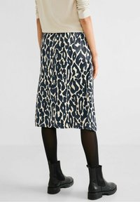 Leopardmönstrad kjol med en krämig bas och ett mörkblått mönster, med en slät textur och en medellång design, som är ihopparad med svarta ankelskor.