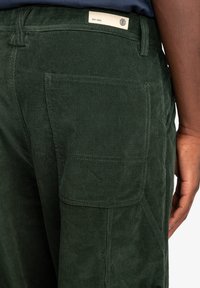 Groene corduroy broek met een gestructureerde oppervlakte, zichtbare zakken en een label aan de tailleband. Het ontwerp heeft stevige stikdetails.
