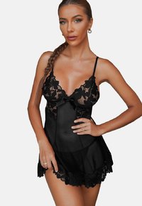 Black sheer babydoll with lace accents, adjustable straps, bow detail at the front, scalloped hemline, and textured floral pattern.