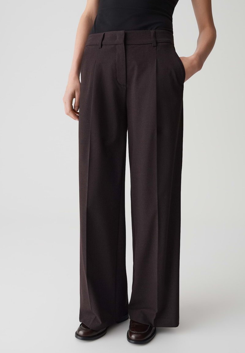 Pantalons à jambes larges en tissu marron foncé, avec une taille plate, des plis, des poches latérales et une coupe ajustée. Texture lisse, design minimaliste.
