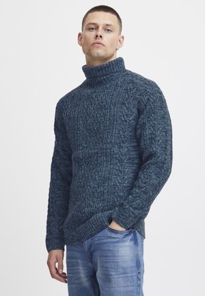 Strikket turtleneck genser i mørkeblå. Strukturert mønster med ribbestrikkede mansjetter og kant. Kombinert med lyseblå jeans.