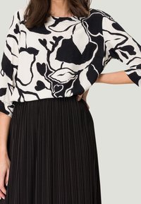 Top de patrón floral en blanco y negro con un corte holgado y mangas anchas, combinado con una falda negra plisada, que exhibe una tela suave y texturada.