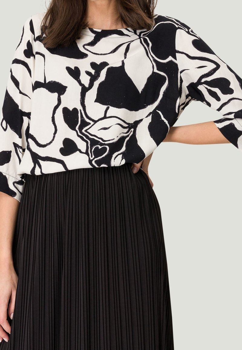 Top de patrón floral en blanco y negro con un corte holgado y mangas anchas, combinado con una falda negra plisada, que exhibe una tela suave y texturada.