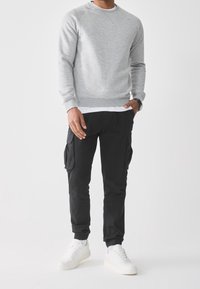 Szary sweatshirt z okrągłym dekoltem, w połączeniu z czarnymi spodniami cargo z bocznymi kieszeniami i białymi sneakerami. Prosty, codzienny strój.