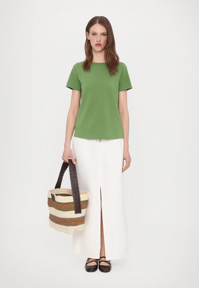 Green short-sleeve shirt, white maxi skirt with front slit, woven striped bag in cream, brown, and green, and dark shoes with straps.