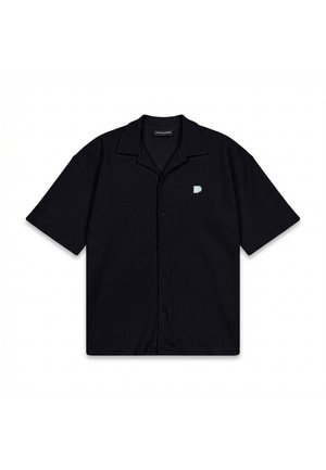 Camisa negra de manga corta con botones y cuello, con un pequeño logo blanco en forma de "P" en el pecho izquierdo, extendida sobre un fondo blanco.