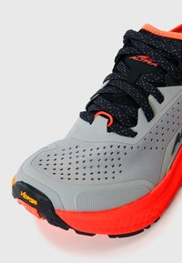 Baskets de course grises avec un dessus texturé, lacets noirs, accents orange et semelle extérieure Vibram. Présente une pointe conique et un design perforé.