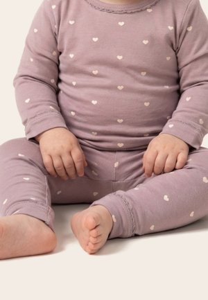 Beebi istub risti jalgadega, kannab lavendlivärvi pikkade varrukatega pidžaamat, millel on väikesed valged südamed heledal taustal.