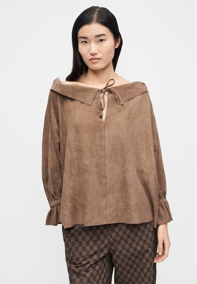 Καφέ μπλούζα από σουέντ με σχέδιο που αφήνει τους ώμους ακάλυπτους, δέσιμο στον λαιμό και σούρες στα μανίκια. Η υφή είναι απαλή με διακριτική γυαλάδα.