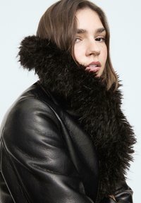 Čierny kožený kabát v kombinácii s hrubým, nadýchaným čiernym šálom. Šál má textúrovaný, mäkký materiál. Celkový vzhľad je moderný a teplý.