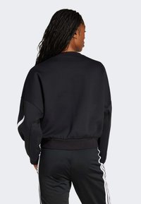 Black oversized sweatshirt with a ribbed waistband, featuring contrasting white stripes on sleeves and a smooth texture, shown from the back.