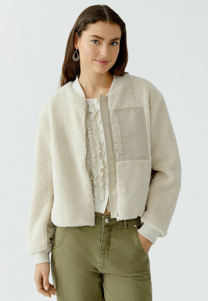 Fleece bomberjack in off-white met een beige nylon paneel. Voorzien van een ritssluiting aan de voorkant, geribbelde manchetten en een borstzak. Draagt over een gerimpeld top.
