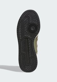Black rubber shoe sole with textured zigzag pattern, featuring an embossed logo and circular detail. Gray and olive green accents visible at edges.