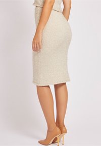 Strickbleistiftrock in hellbeige mit strukturiertem Finish, in taillierter Form und mit ausgefranstem Saum, kombiniert mit hellbeigen High Heels.