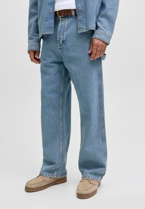 Light blue denim jacket and jeans with a loose fit, featuring white stitching and a brown leather belt. Beige moccasin shoes.