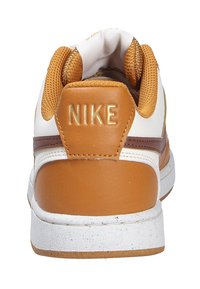 Sneaker Nike avec un dessus en cuir blanc, des accents en cuir beige et une bande marron. Le talon présente l'inscription "NIKE" embossée en doré.