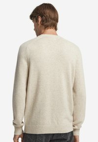 Jasno beżowy sweter wykonany z miękkiego dzianiny. Posiada okrągły dekolt, ściągacze na rękawach i dół, a także prostą, gładką teksturę.
