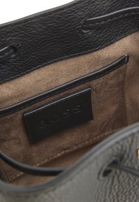 Mustast nahast käekoti sisemus beežist seemisnahast voodriga, millel on kaarditasku, reljeefsete logodega lõige ja kontrastsed õmblused.