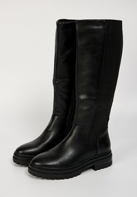 Bottes en cuir noir, arrivant aux genoux, avec une finition lisse, une fermeture éclair sur le côté et un panneau élastique pour plus de flexibilité. Semelle en caoutchouc robuste pour une meilleure adhérence.