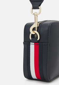 Borsa in pelle blu navy con una texture liscia, caratterizzata da una cerniera dorata e una tracolla con strisce rosse, bianche e blu.