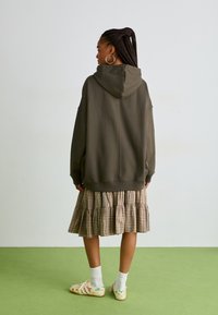 Felpa oversized verde scuro, gonna a balze in beige e marrone, calze bianche e scarpe con motivo, viste da dietro.