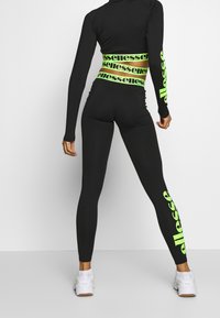 Svart träningsset som innehåller en figurnära långärmad topp och högmidjade leggings. Klara gröna ”ellesse” logotypdetaljer på midjebandet och benen.