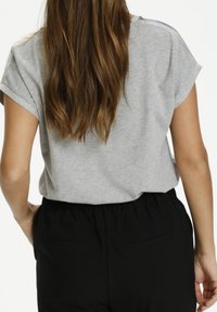 T-shirt gris à manches courtes retroussées, associé à un pantalon noir à taille élastique avec poches arrière. Texture douce semblable au coton.