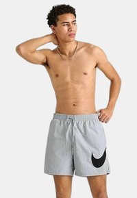 Pantaloni da bagno grigio chiaro con vita elasticizzata, chiusura con cordino e un grande logo Nike nero sul lato sinistro.