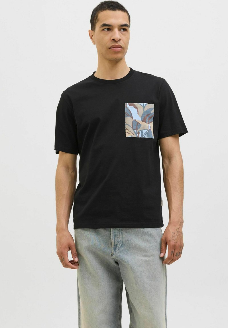 Sort bomulds t-shirt med en mønstret lomme i blå, beige og brune nuancer. Korte ærmer og en afslappet pasform.