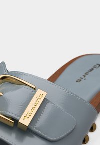 Ανοιχτό μπλε δερμάτινο σανδάλι slide με μεγάλο χρυσαφί αγκράφα και ξύλινη σόλα, με την επωνυμία «Tamaris» στην αγκράφα και στην εσωτερική σόλα.