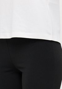 Hvit bomulls t-skjorte med avrundet kant, kombinert med svarte leggings. T-skjorten ser myk ut, og leggingsene har en glatt, elastisk tekstur.