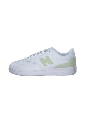 Zapatillas blancas con una parte superior de cuero suave, que presentan un acento de ante verde claro en el talón y una puntera perforada para mayor transpirabilidad.