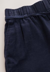 Navy blue linen pants featuring an elastic waistband, gathered texture, and side pockets, with a soft, lightweight feel.