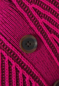 Pulsante scuro cucito su tessuto lavorato a maglia rosa e bordeaux con motivi intrecciati e a coste.