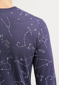 Camicetta a maniche lunghe blu navy in cotone, con equazioni matematiche e forme geometriche bianche stampate in diverse dimensioni su tutta la stoffa.