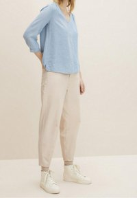Blusa a righe blu chiaro con scollo a V e maniche a tre quarti, abbinata a pantaloni beige a tubo e sneaker alte bianche.